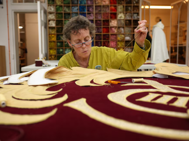Senior studio embroiderer Helen Stevens hand‑stitches the royal cypher of Britain's King Charles/REUTERS