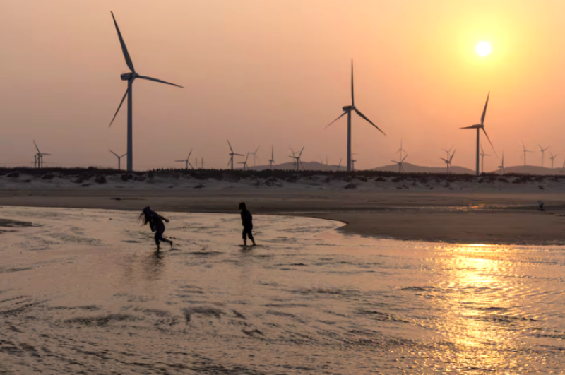 people walk past wind turbines at a beach on the taiwan strait during sunset on pingtan island fujian province china april 10 2023 photo reuters